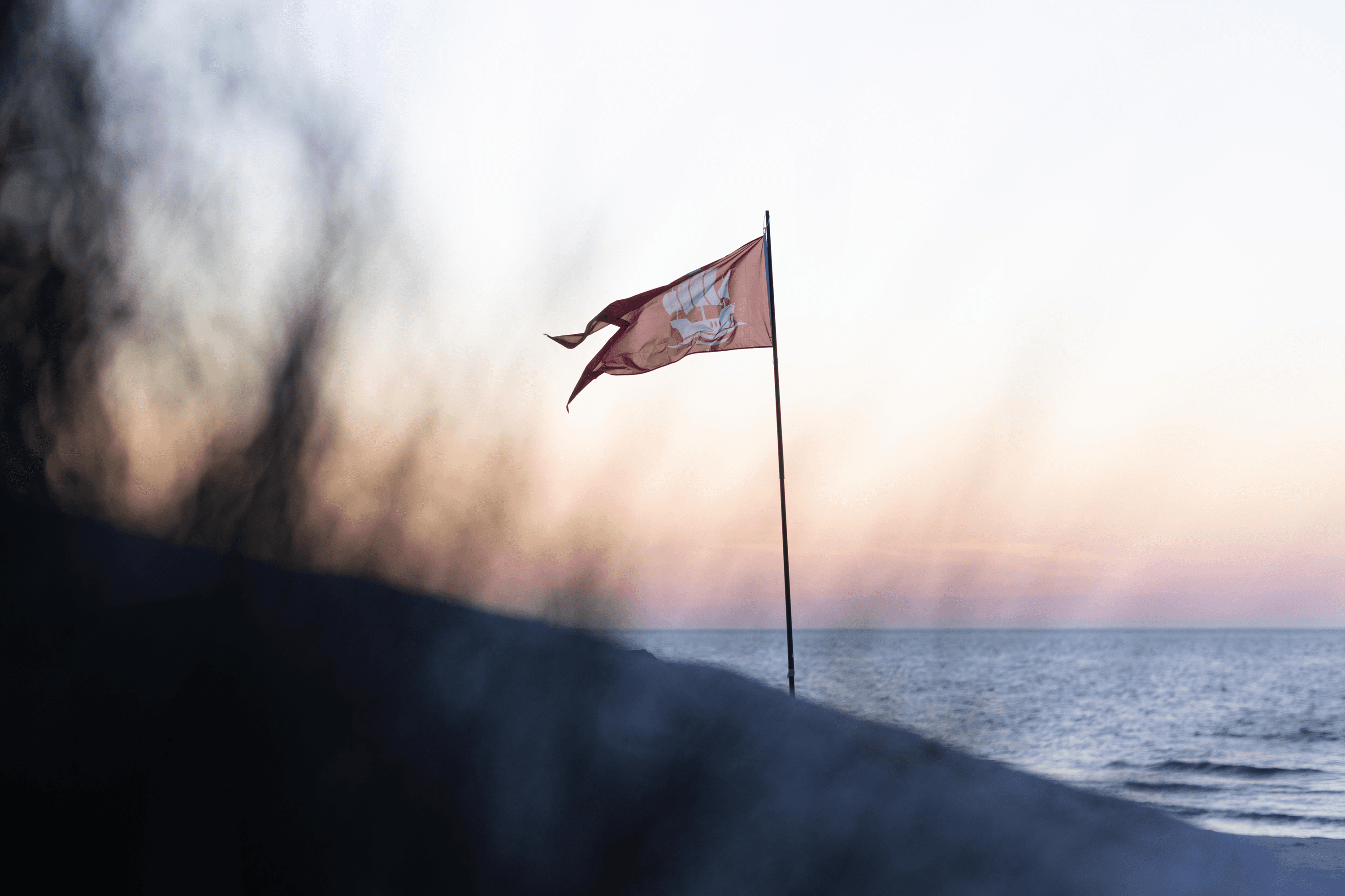 Flag with ship silhouette on beach at sunset
