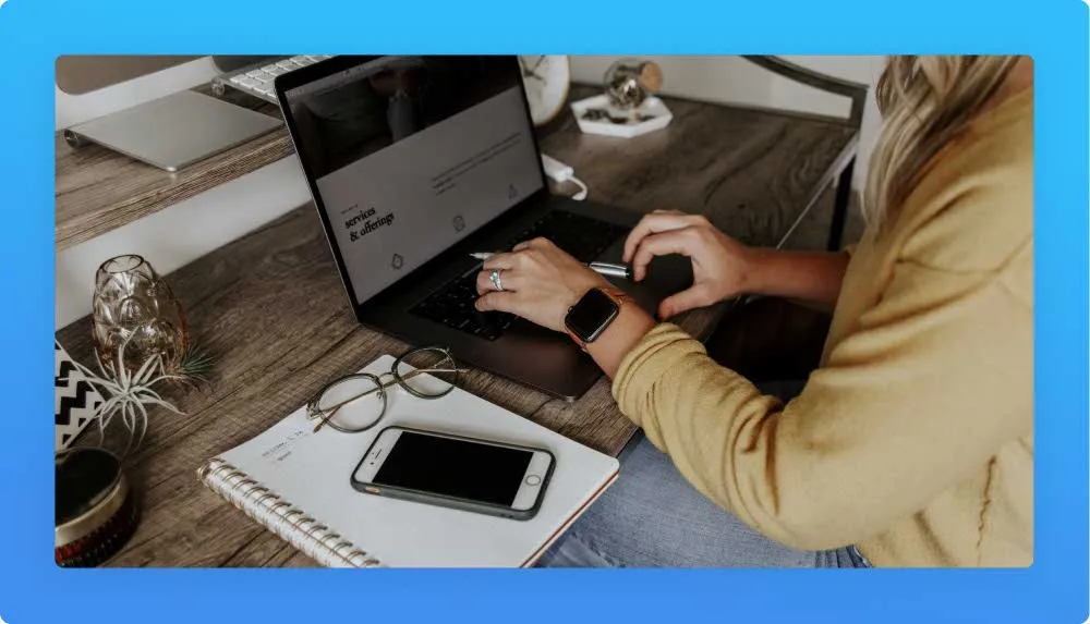 Woman writing website content at her laptop. At her left side, notebook, glasses and mobile phone