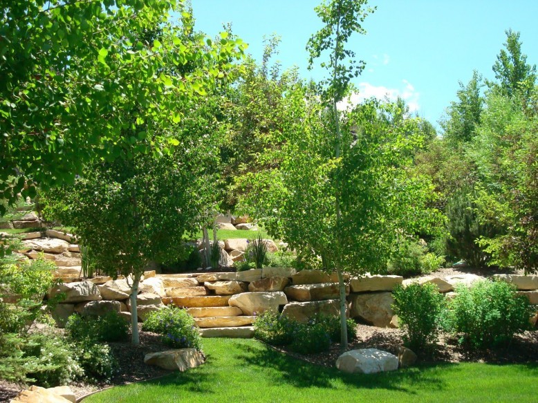 backyard with aspen trees in the front yard, surrounded by large boulders, outdoor seating area with stone steps