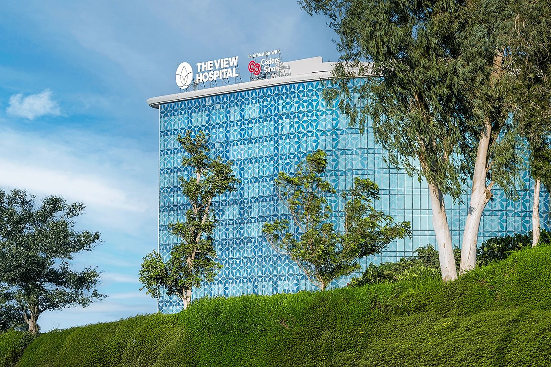 The View Hospital, un hôpital privé de Doha, sa façade de verre bleu à motifs géométriques entourée d'arbres, de ceux qu'une assurance santé ouvre au Qatar