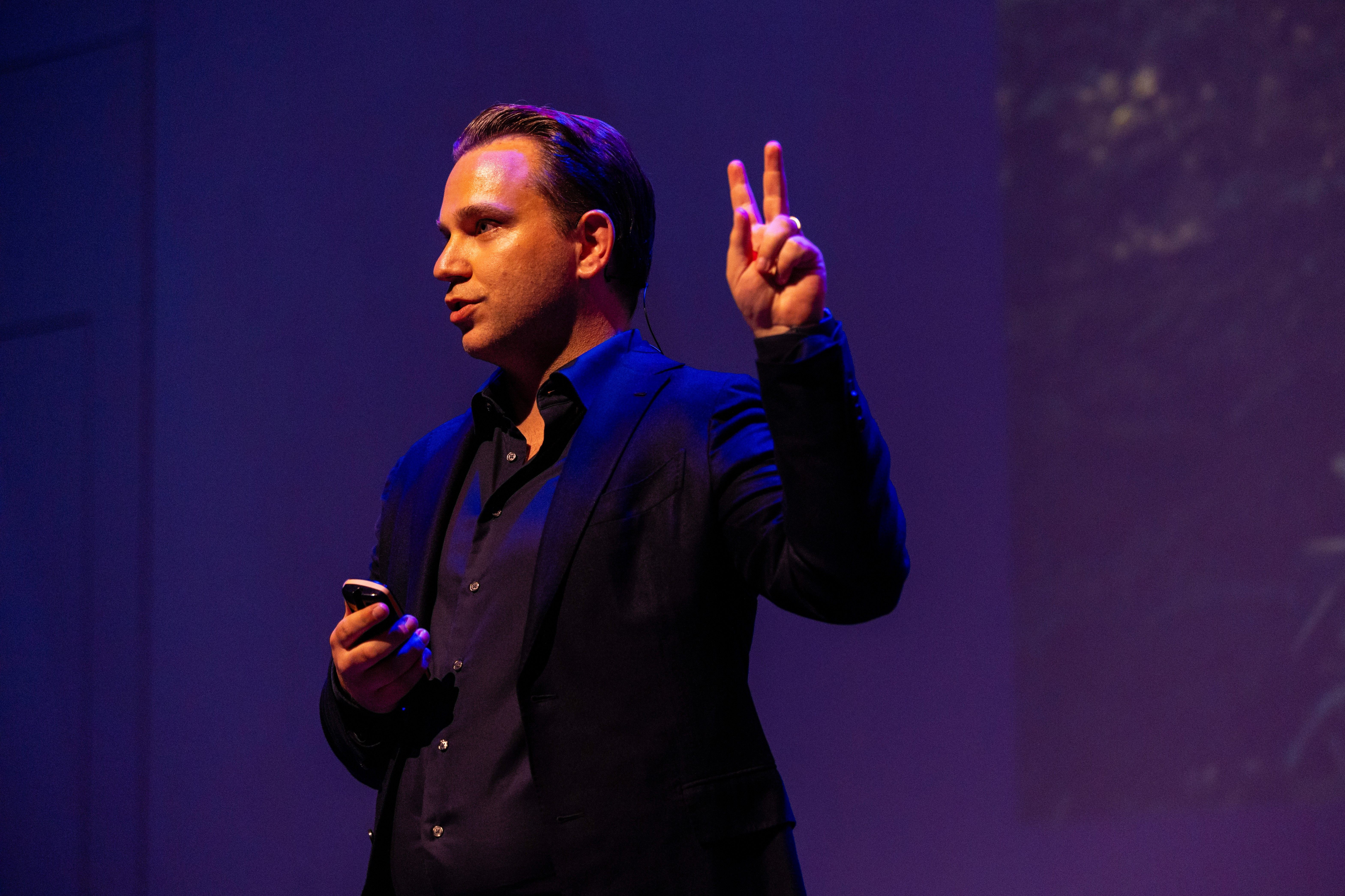 A smiling young man with crossed arms, wearing a plaid shirt and white t-shirt, poses against a dark background.