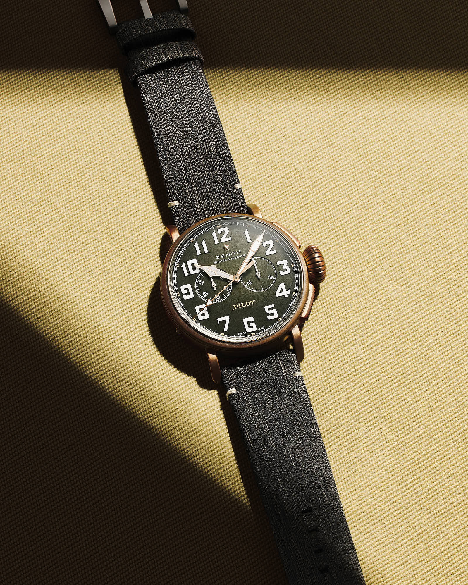 Luxury Zenith pilot watch with black leather strap on sunlight background.