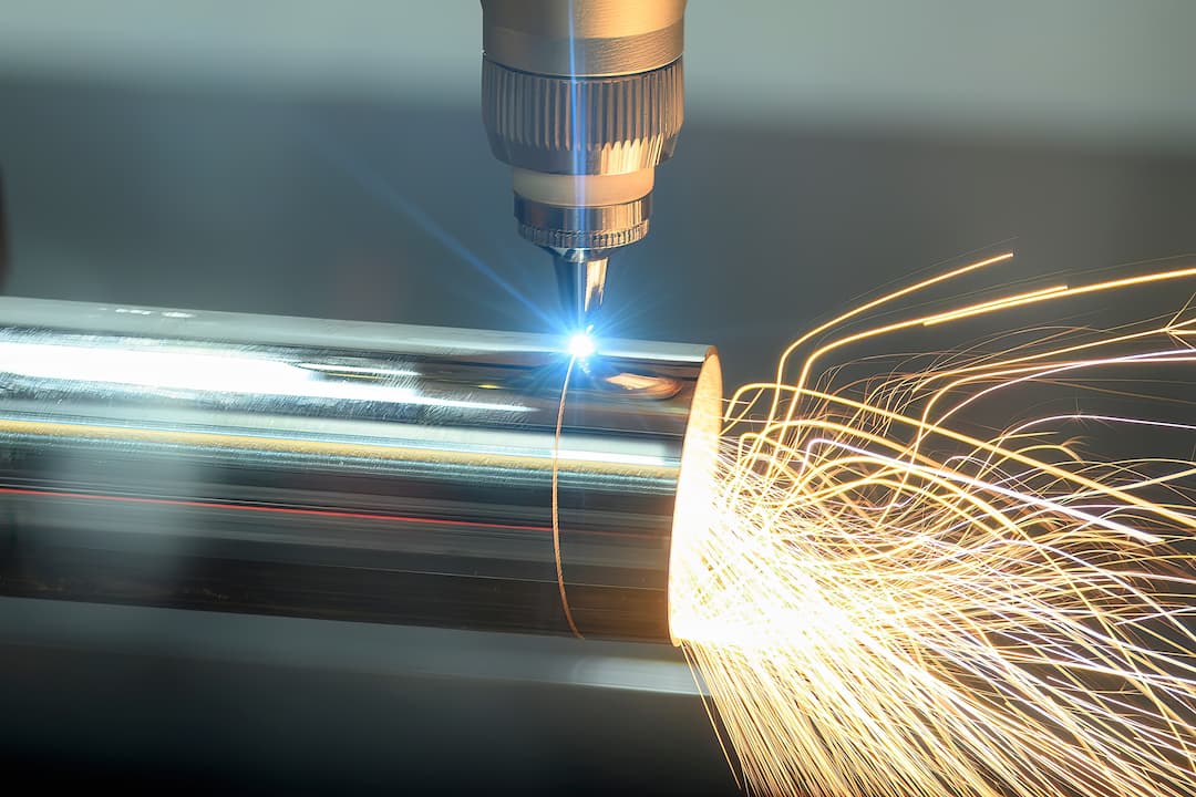 A high-precision laser cutting a stainless steel pipe with sparks in an industrial setting.
