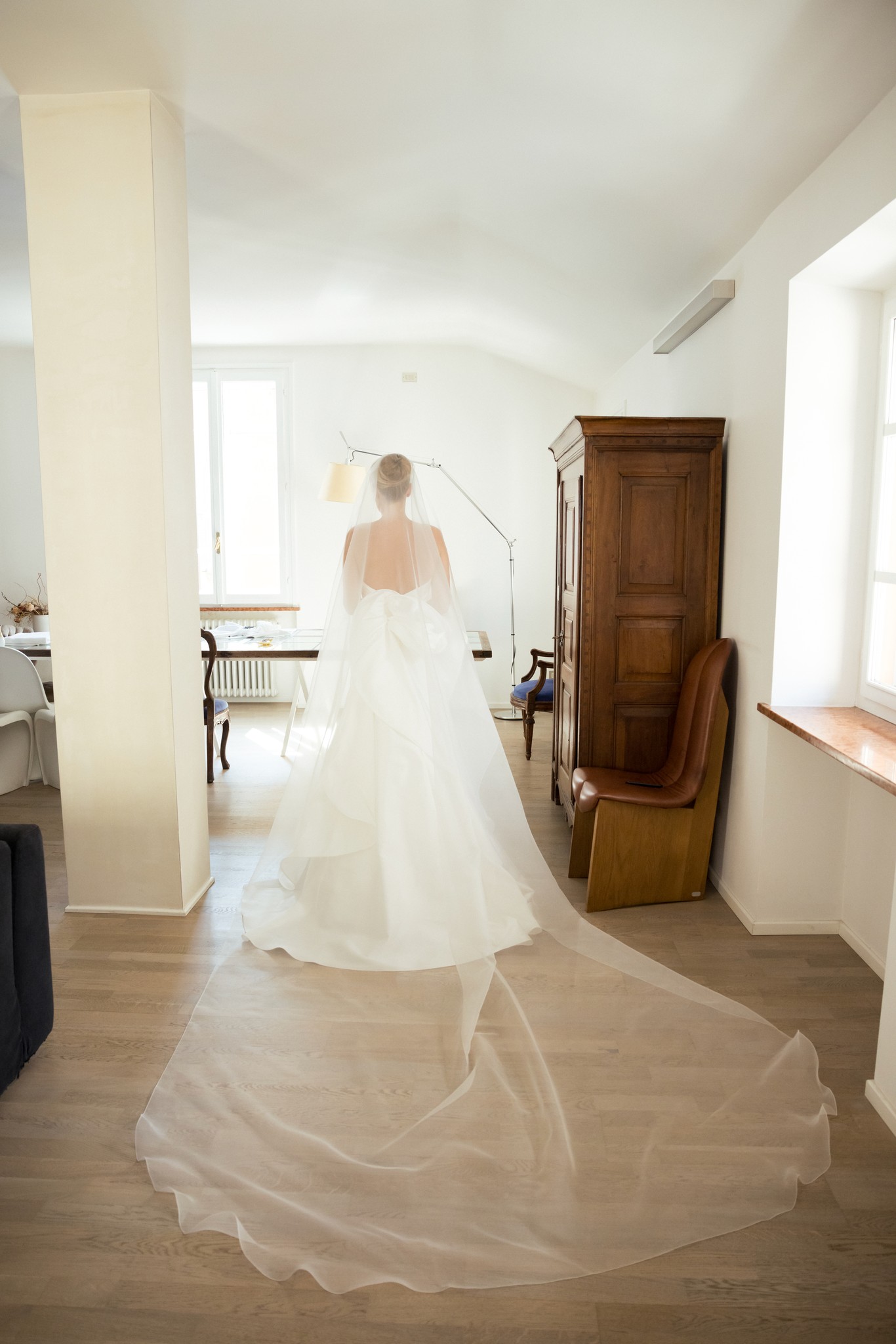 Sposa di spalle nel vestito da matrimonio con velo a strascico, in piedi presso Villa Malenchini, luce naturale da finestra