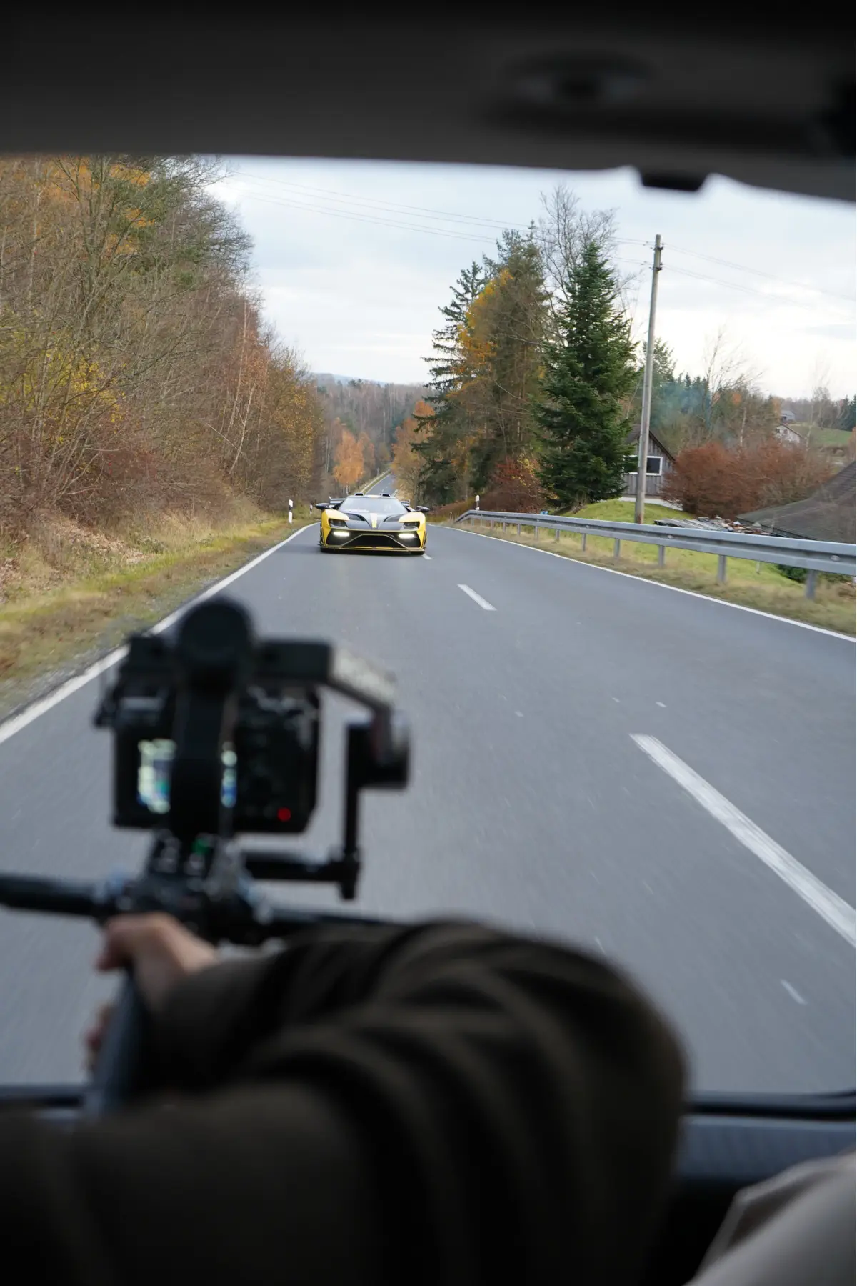 Behind the scenes shot of a yellow Mansory car in motion with a cameraman filming from the trunk using a stabilizer