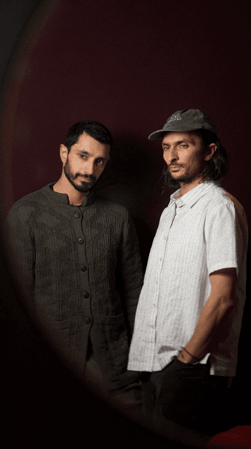 Bride sitting on ground against wall, groom standing nearby