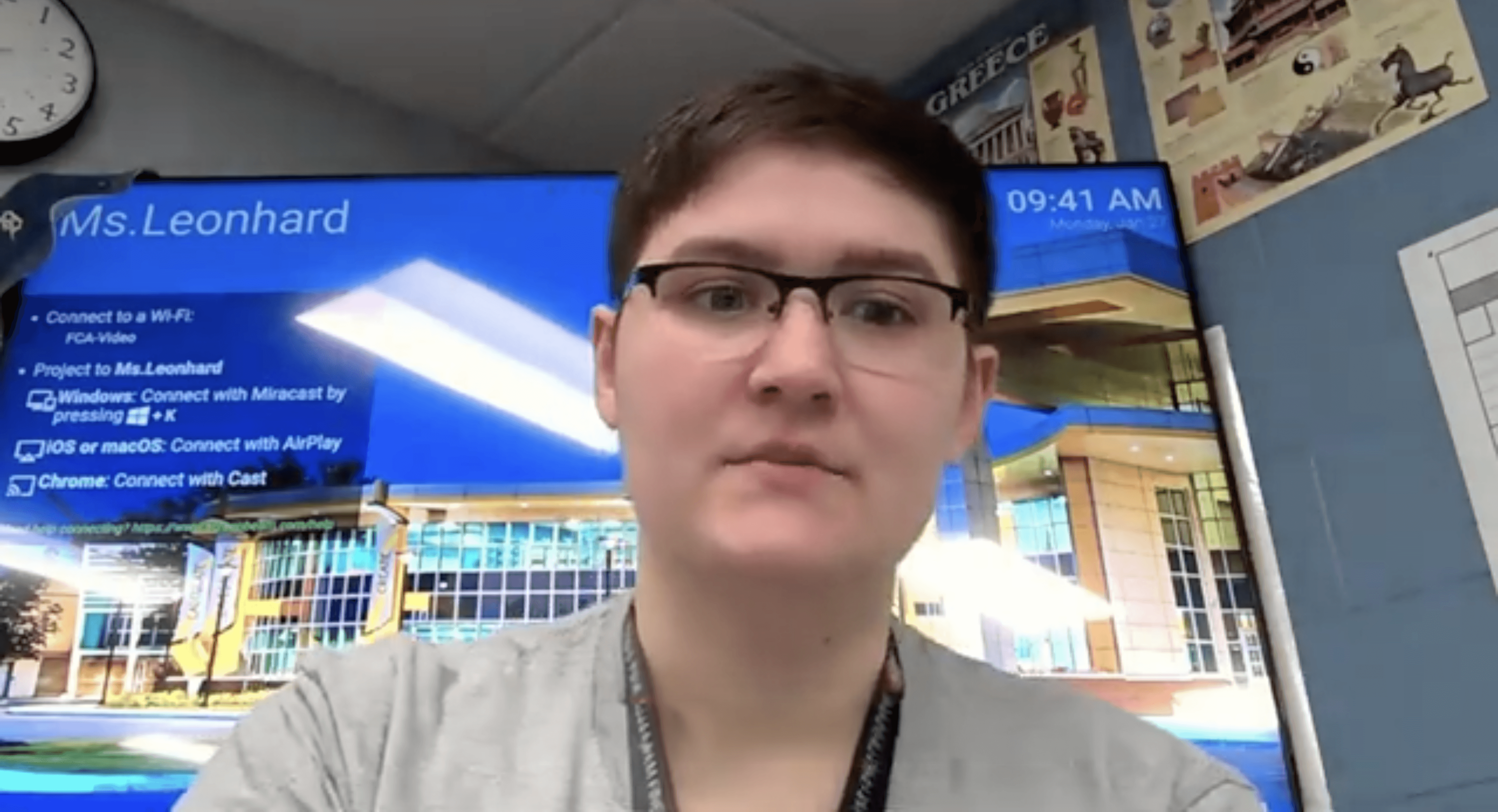 A young woman with long dark hair stands outdoors at night beside a blue vehicle. She is wearing a black athletic-style jersey with white stripes and graphic elements on the front. The background shows softly lit buildings and warm lights, suggesting an urban setting. She appears to be mid-step, looking slightly to the side with a composed expression.