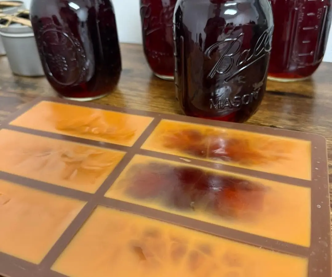 Four glass mason jars filled with rich, dark liquid are placed on a wooden surface alongside a silicone mold used for soapmaking in Bradenton, FL.