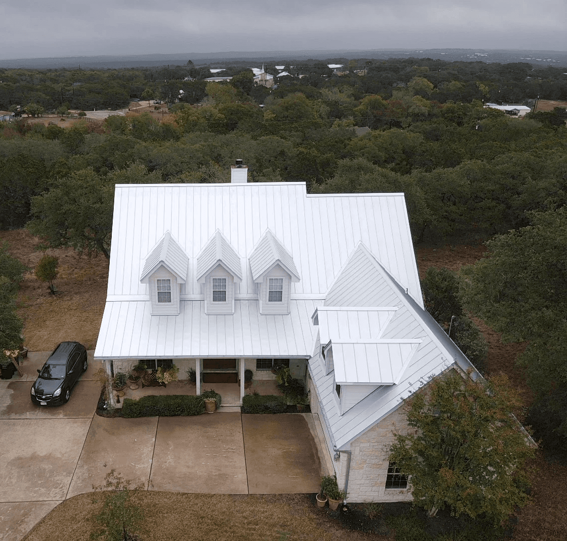 Beautiful Dripping Springs home with a standing seam Galvalume crossed hip roof, featuring dormers and newly installed gutters for a polished and functional look.