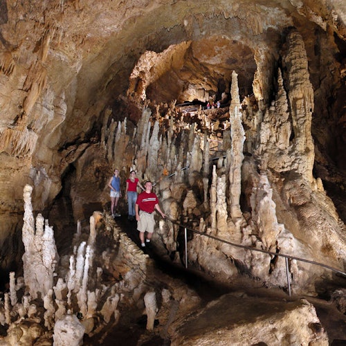 Several people explore a cave with numerous stalagmites and stalactites, using a pathway with railings for safety.