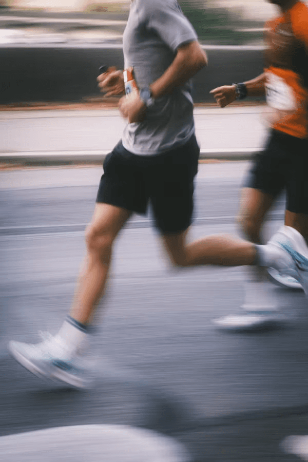 Two runners in motion on a road, dressed in athletic wear, showcasing their legs and sneakers.