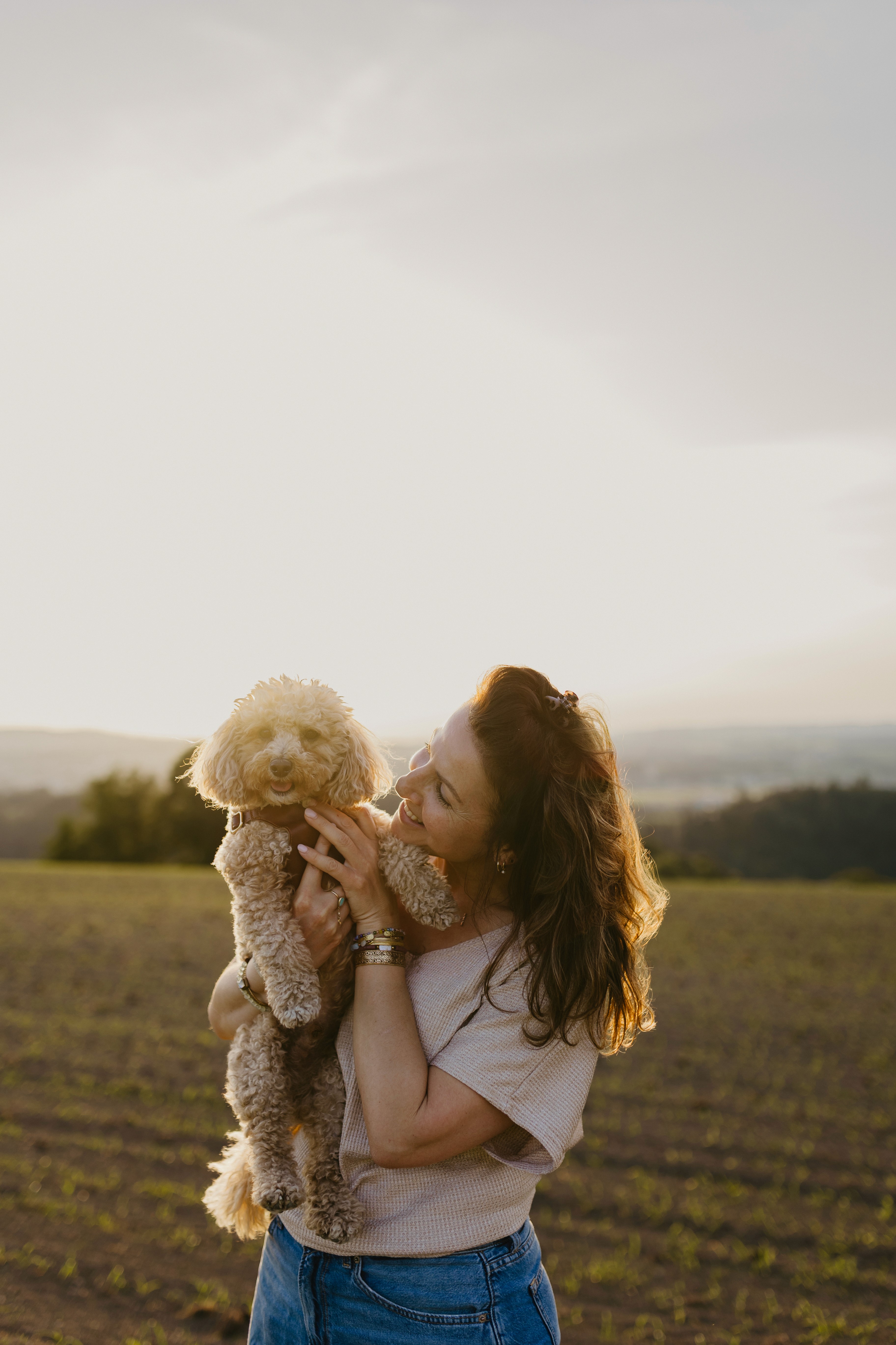 Woman holding her poodle in a field at sunset
