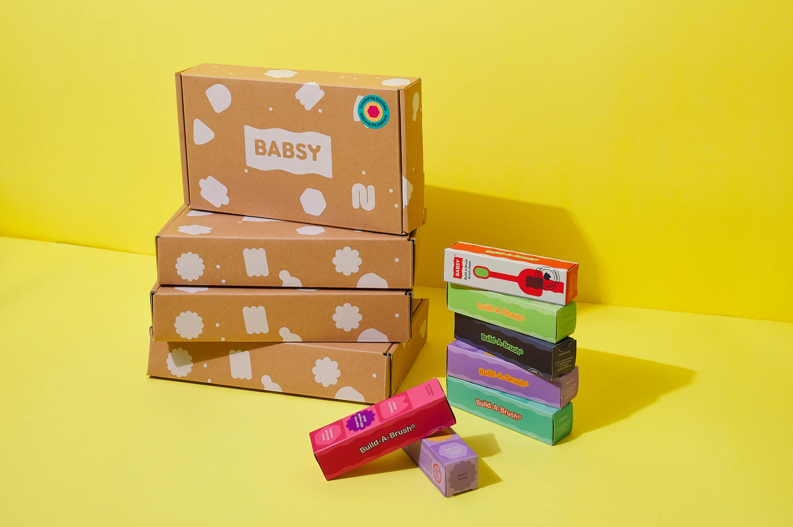 Stacked BABSY Build-A-Brush packaging boxes and colorful component packages on yellow