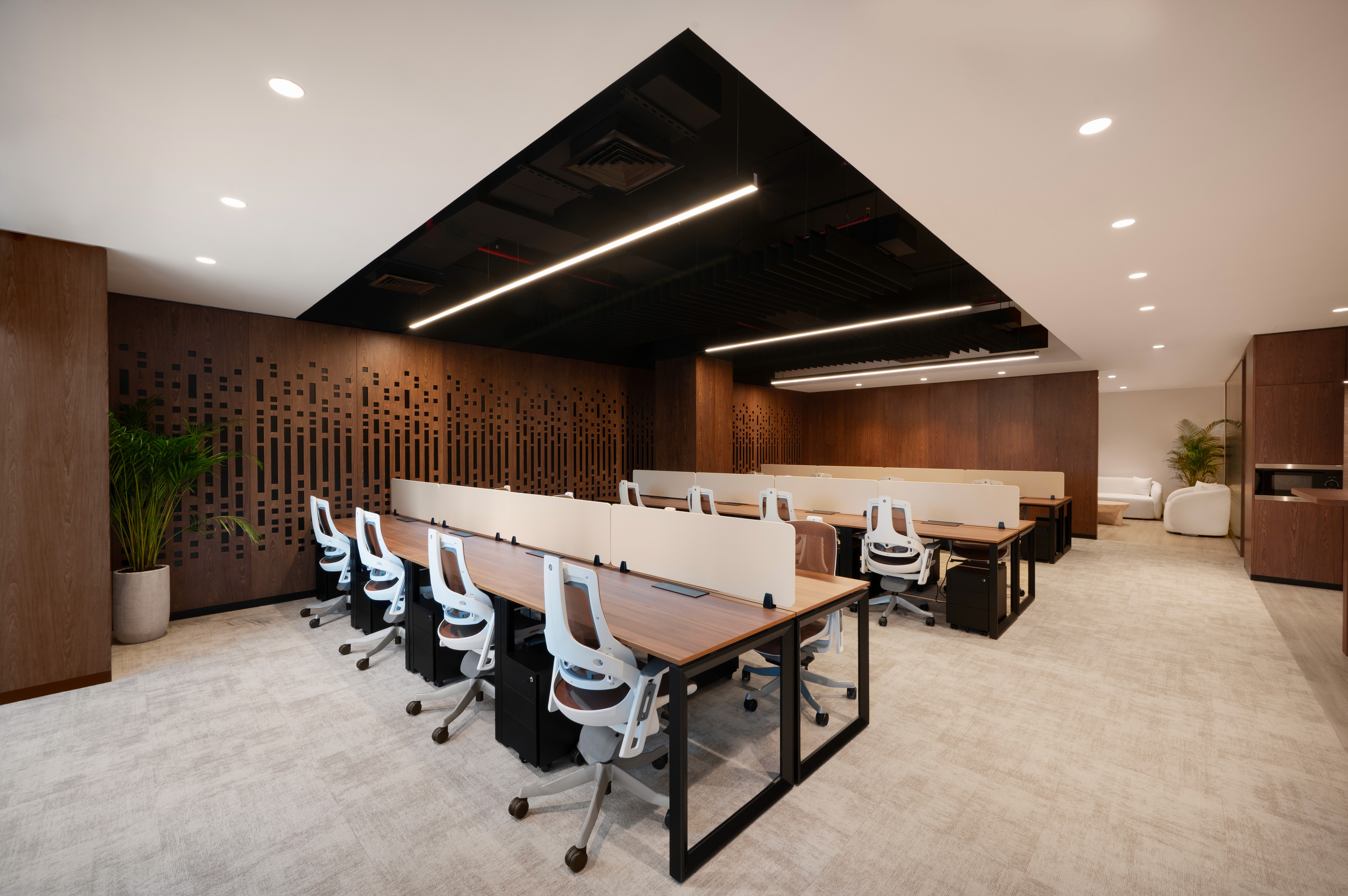 Modern office lounge of Office Square in Dubai with green and beige seating, coffee tables, a wooden bar counter, and integrated café space featuring natural decor and warm lighting.