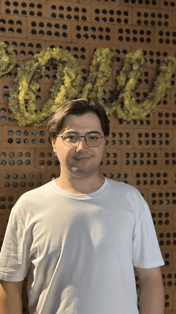 Man with dark hair wearing a black sweater over a collared shirt, softly lit and facing forward
