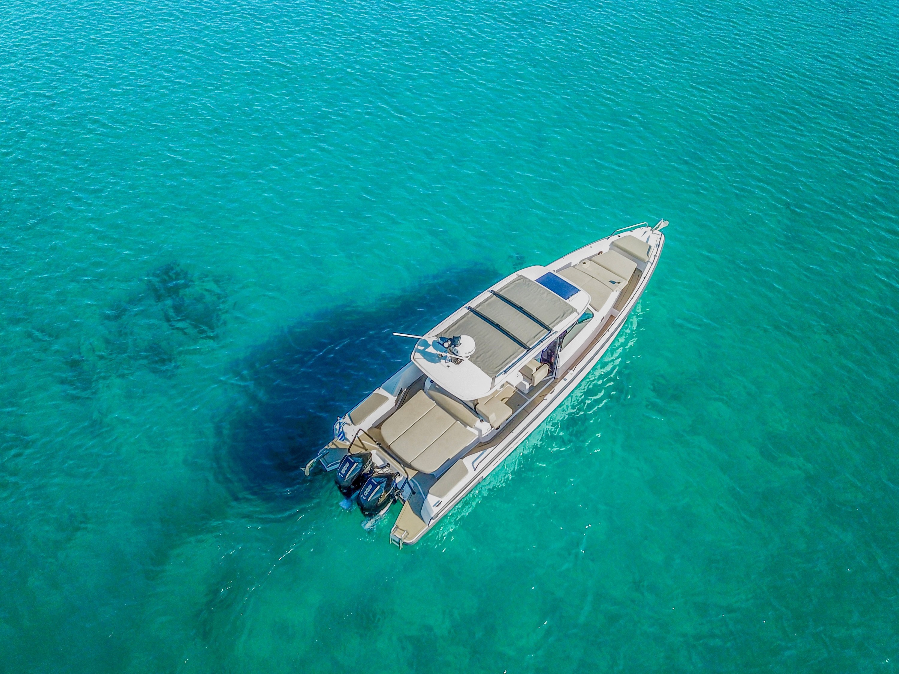 White Axopar 37 Zeus motor yacht anchored in crystal-clear turquoise waters of the Aegean Sea, aerial view.