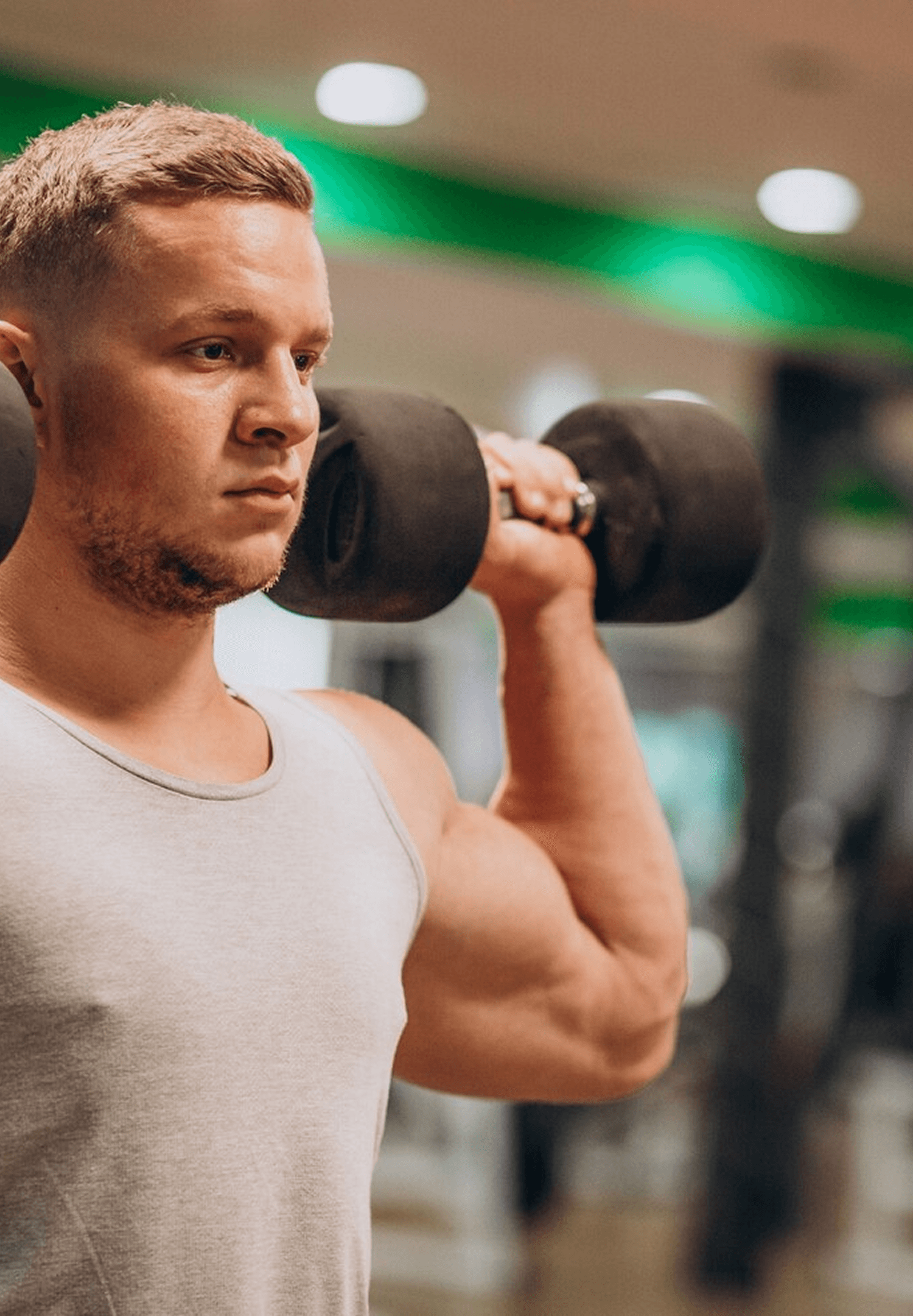 Man lifting a dumbbell on his shoulder in a gym.