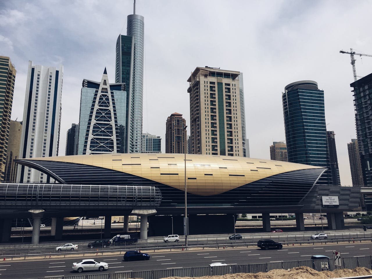 Ein Dubai Metro Zug fährt entlang der beeindruckenden Skyline von Dubai, während im Hintergrund die berühmten Wolkenkratzer und die Palm Jumeirah sichtbar sind. Dieses Bild vermittelt einen Eindruck von der modernen Fortbewegung in der Metropole und dem dynamischen Verkehrssystem der Stadt.