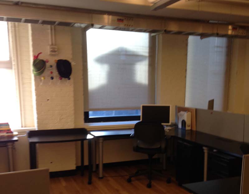 A photo of a desk wit a pc on it. Behind there is a screen with a shadow of a man wearing a graduation robe and hat.