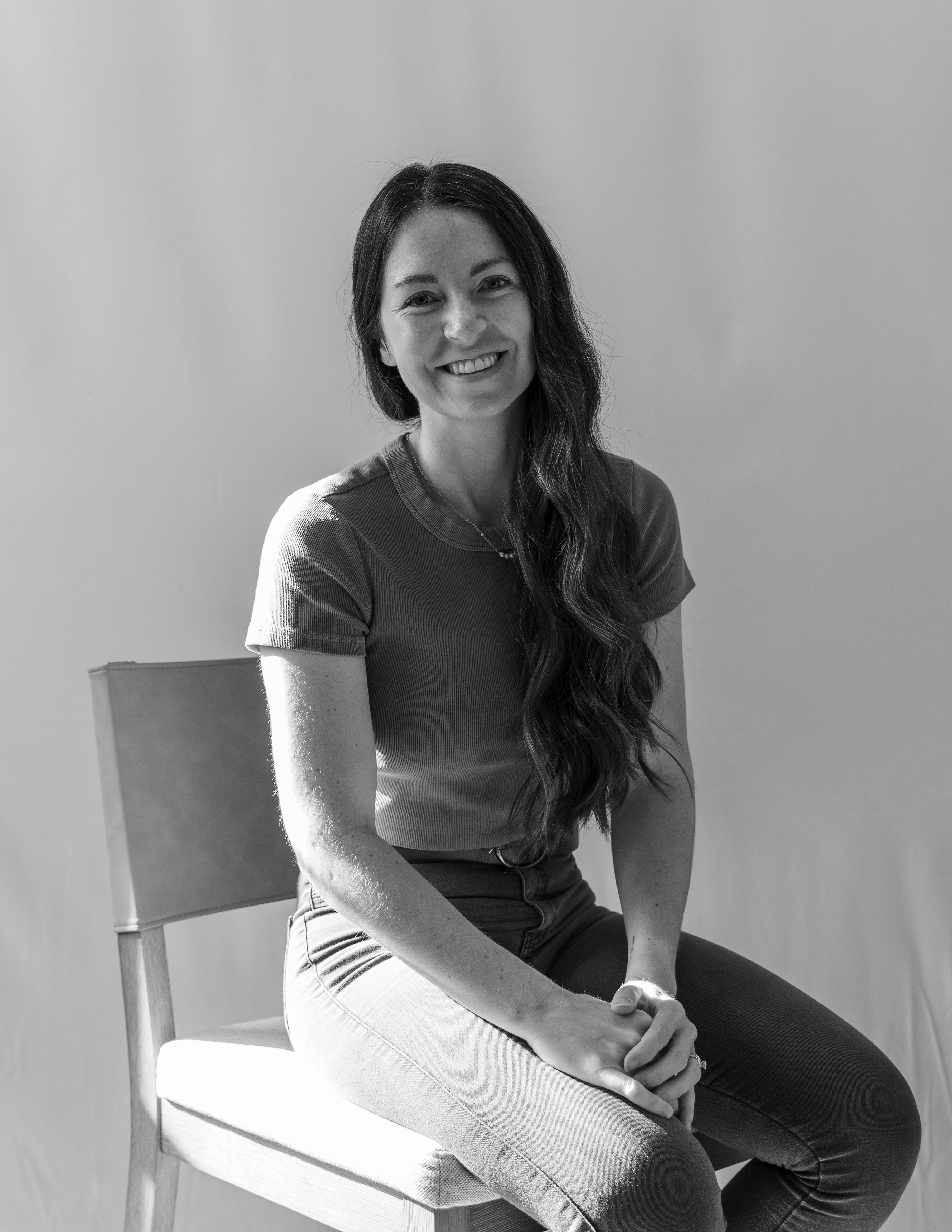 photo of a woman sitting in a chair smiling with a white backdrop behind her