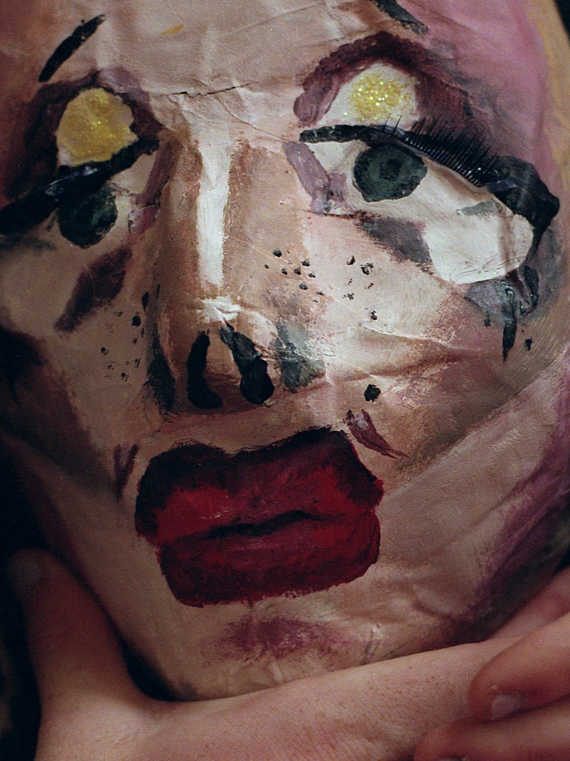 "Paper-mâché mask held in a hand"