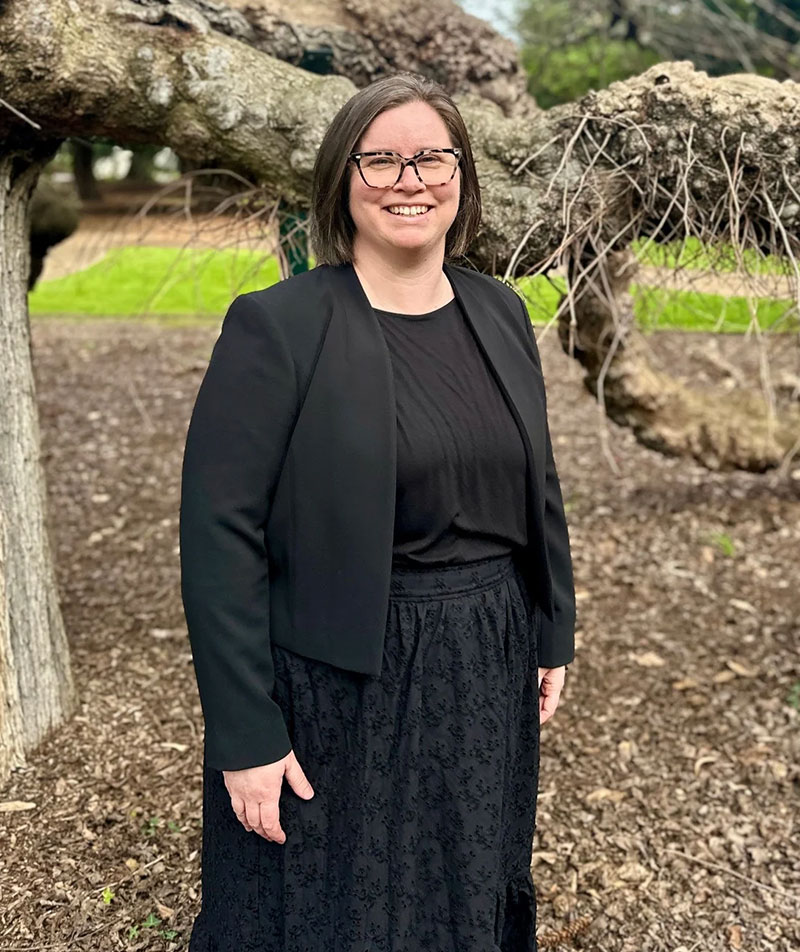 A profile image of Beth Humphries in professional clothing in a leafy outdoor setting