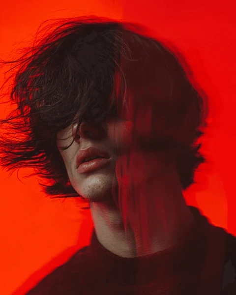 Artistic motion-blurred portrait of a man with messy hair against a solid red background.