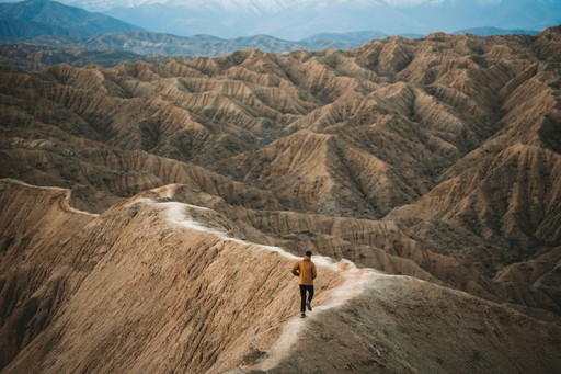 Man running on a winding path through desert badlands.