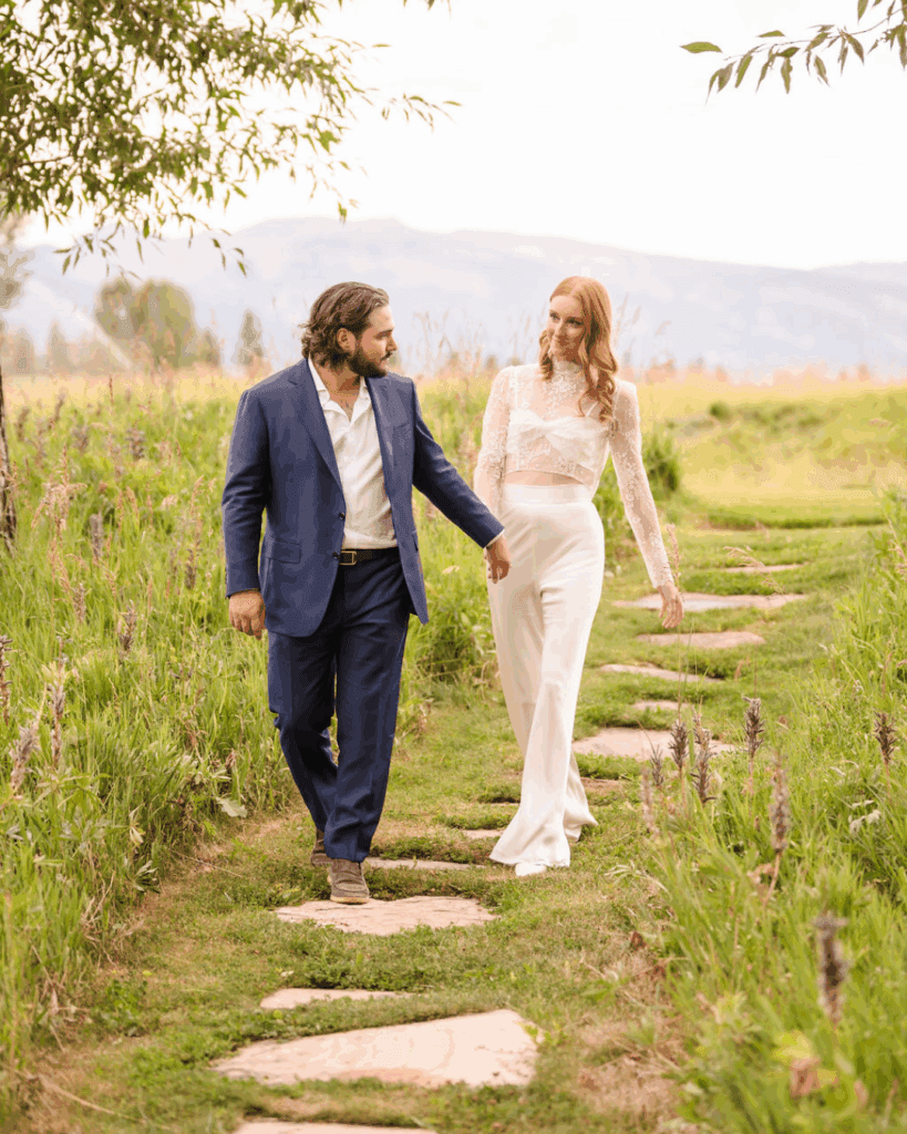 Newlyweds walking along stepping stones through a meadow
