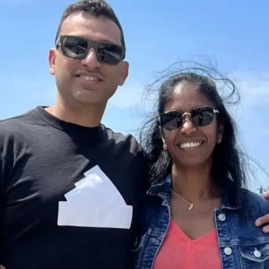 Two people smiling outdoors with sunglasses.