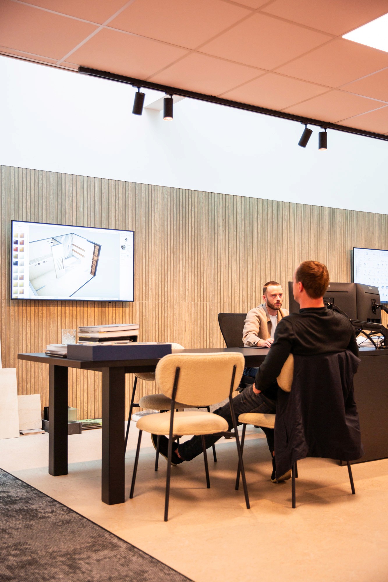 Young man in a green hoodie holding a yellow phone while seated at a table with a tablet.