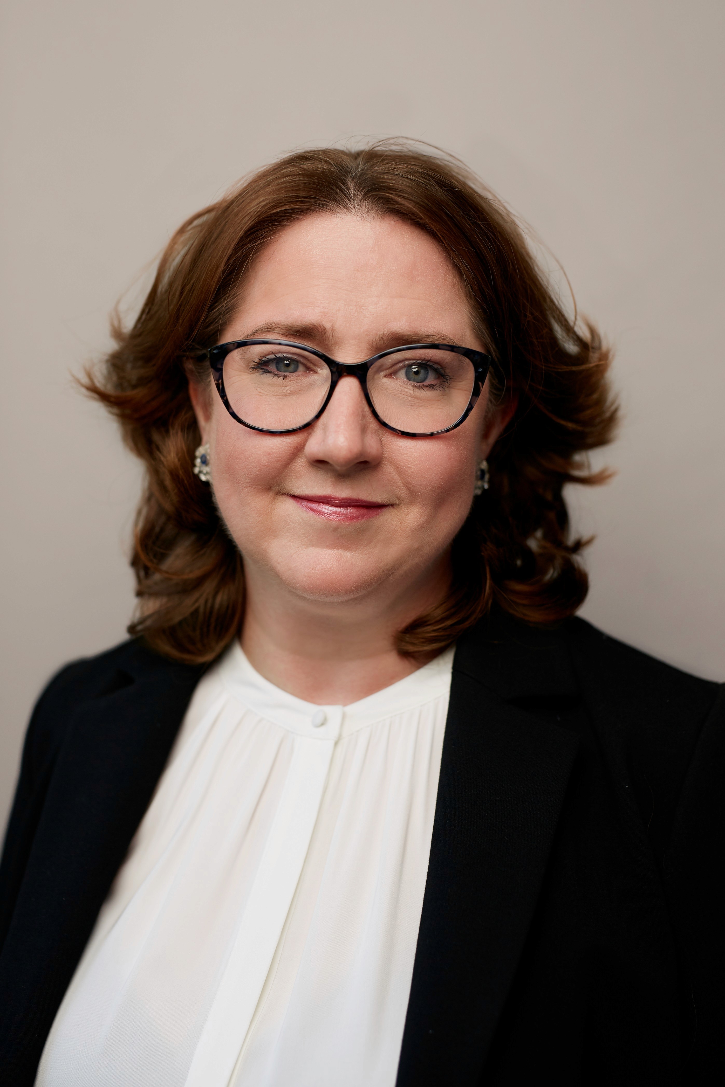 Woman with auburn hair, glasses, and a black blazer.