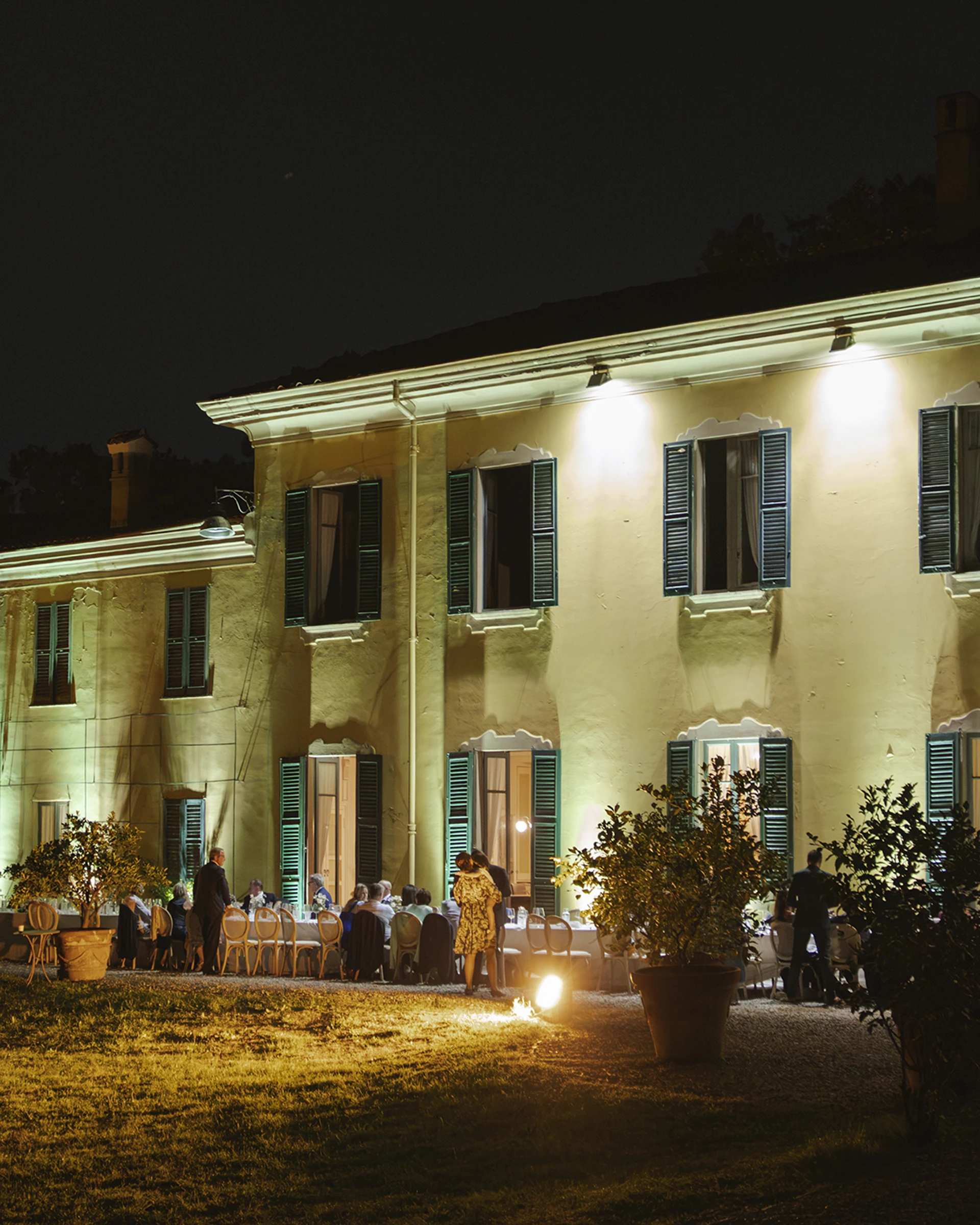 Villa illuminata di sera con gli ospiti seduti a tavola nel giardino
