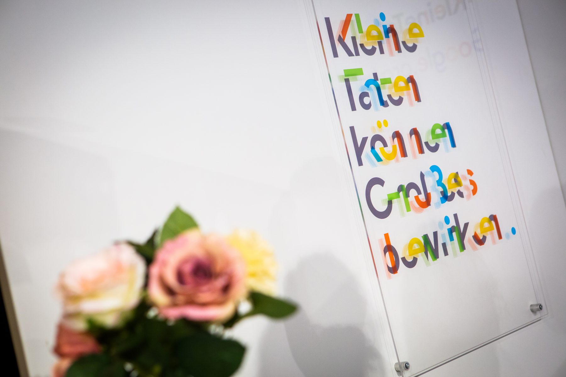 Rosen vor bunter Buchstabentafel mit Schriftzug: Kleine Taten können Großes bewirken