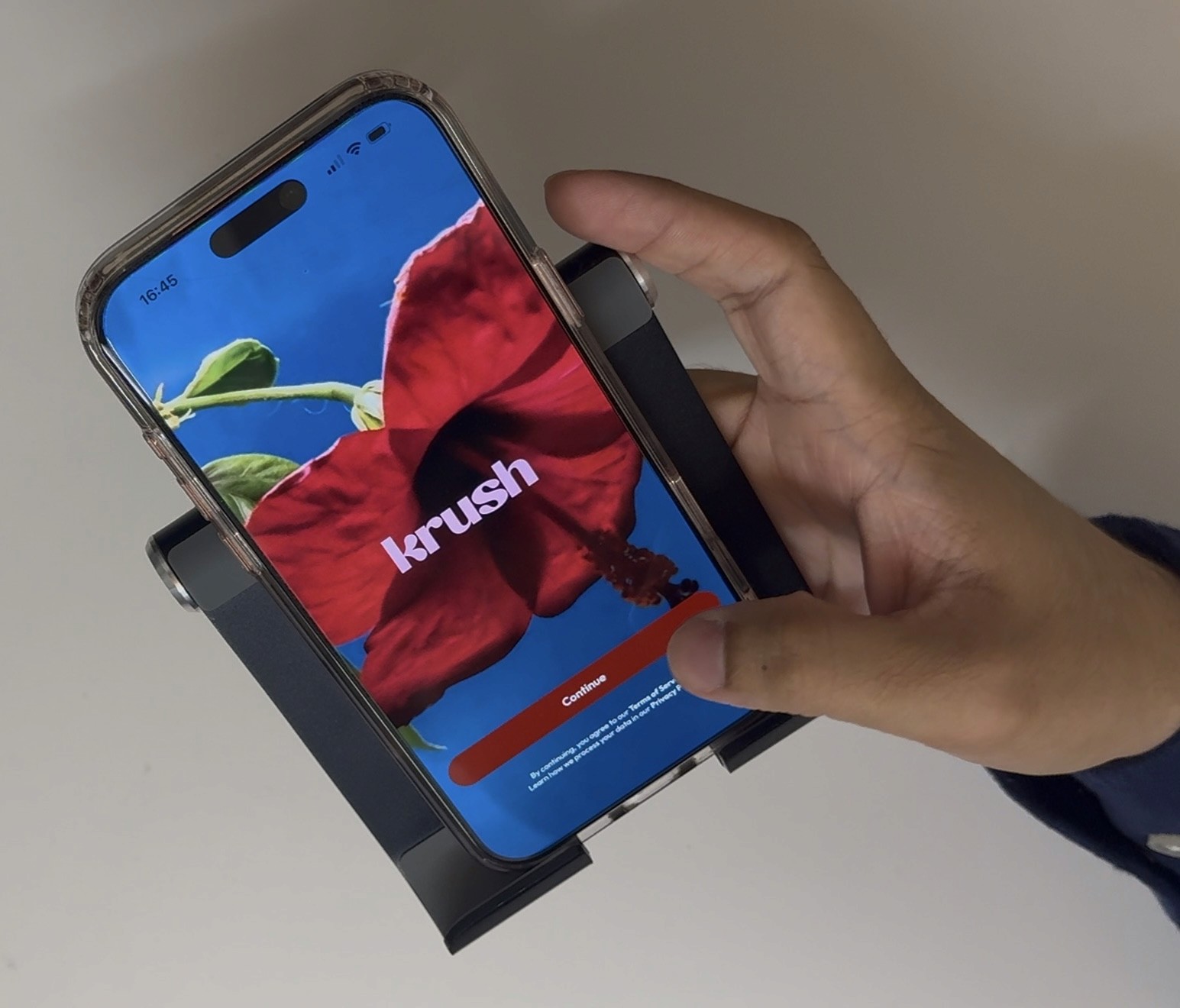 Hand holding a phone mounted in a tripod, displaying KRUSH's red hibiscus splash screen with the brand logo. Captured during a moderated usability session in the Pratt UX Lab.