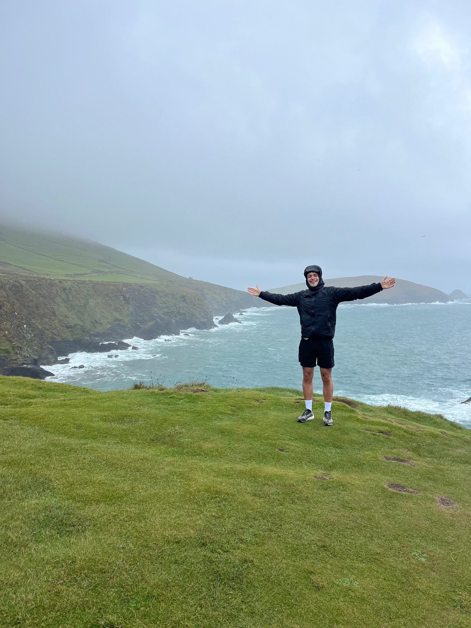An image of Luke - founder of Hamilton Solutions standing at a clif in County Kerry Ireland in the rain while he is smiling with his hands in the air.