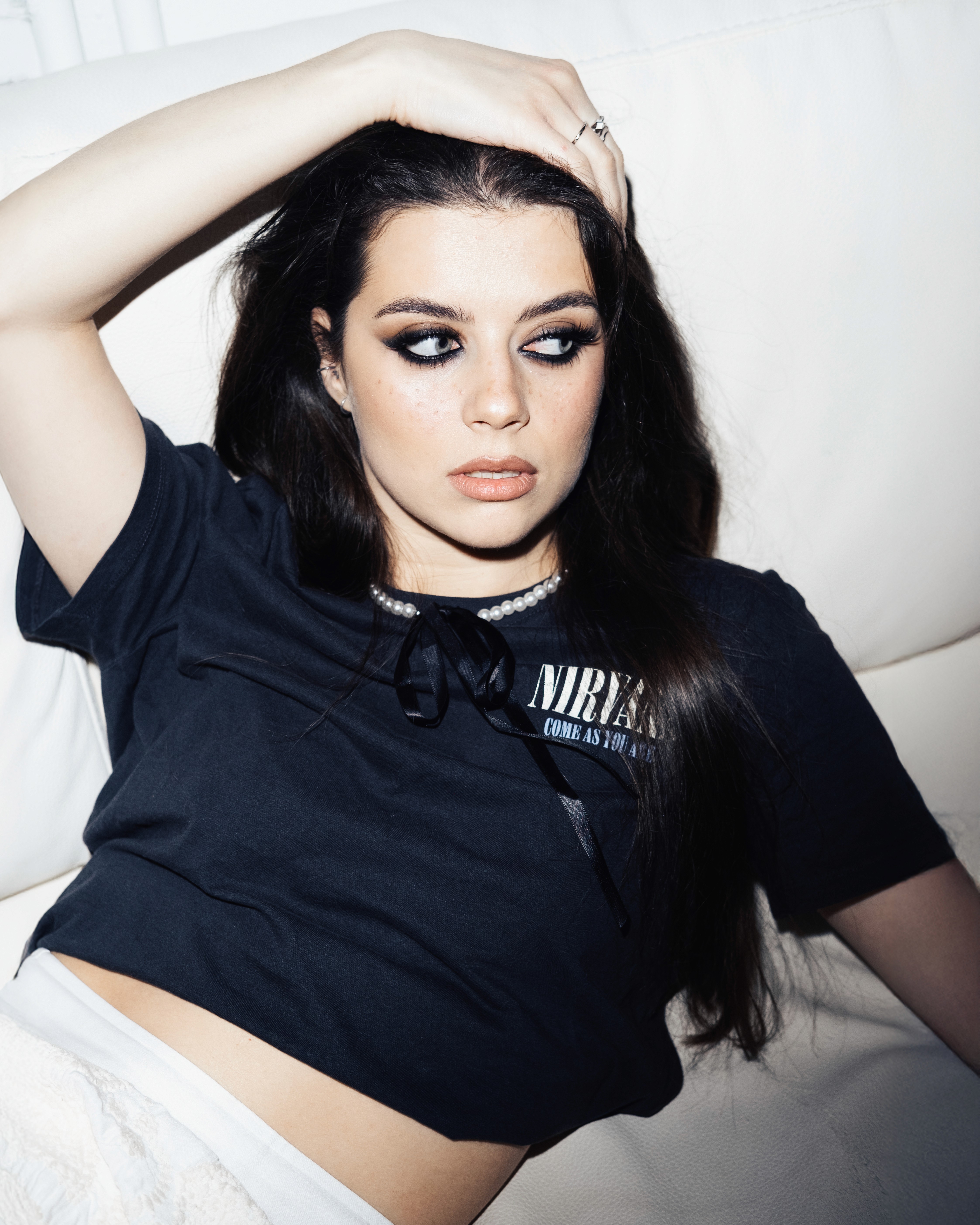 Tanya – Youth Disorder – reclined on a white couch with smoky eye makeup and hand resting on her head