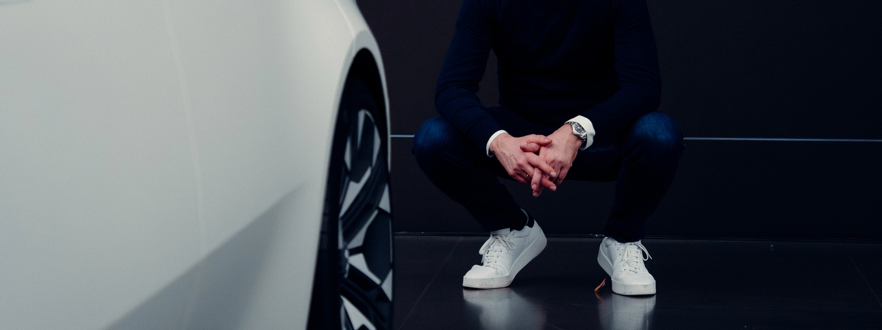 Man kneeling beside a car in a sleek, modern indoor environment with blue accents