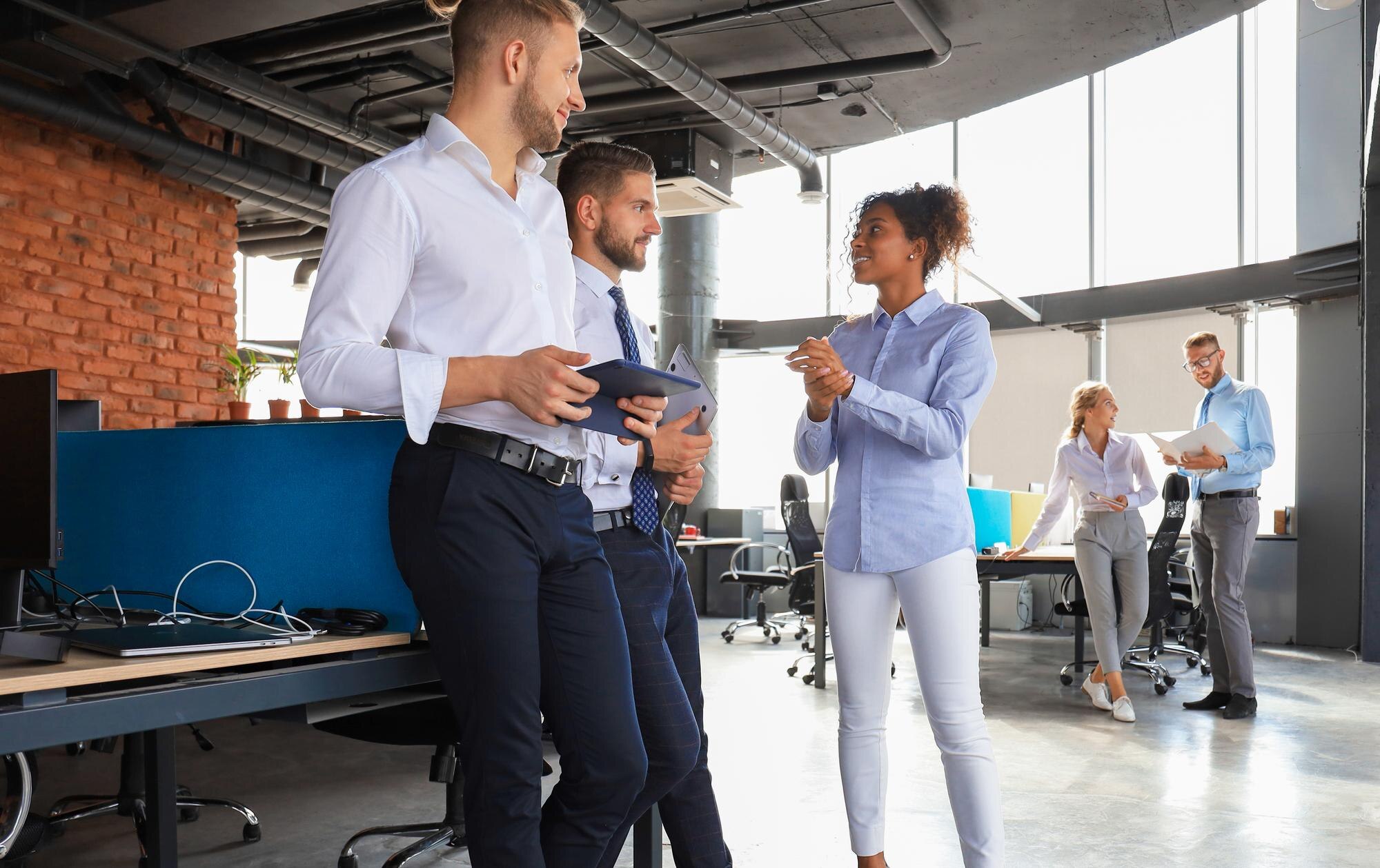 A group of three individuals stand by a desk having an informal meting