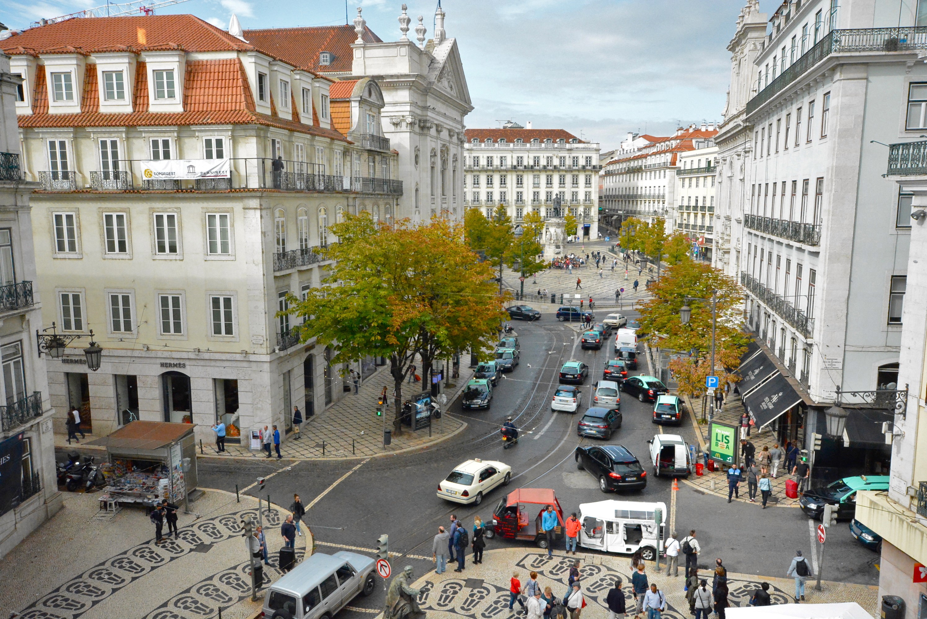 Historic Lisbon buildings along a sunlit street with parked cars and overhead wires.