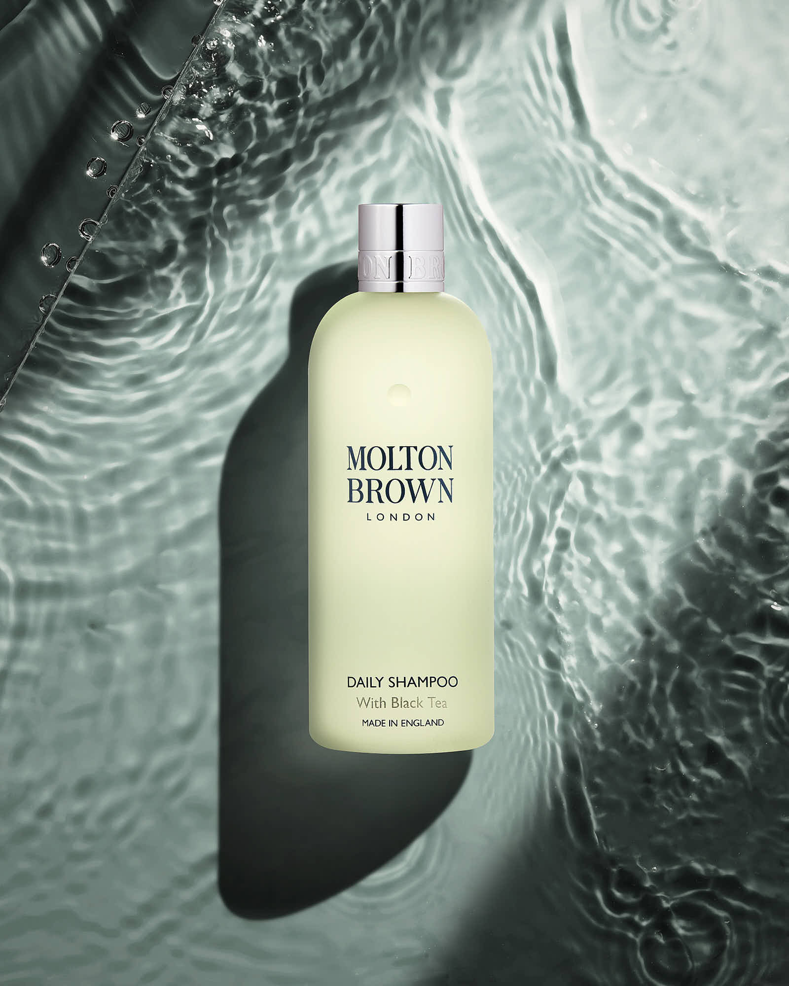 A green bottle of skincare product sits against a textured wall, casting a soft shadow.