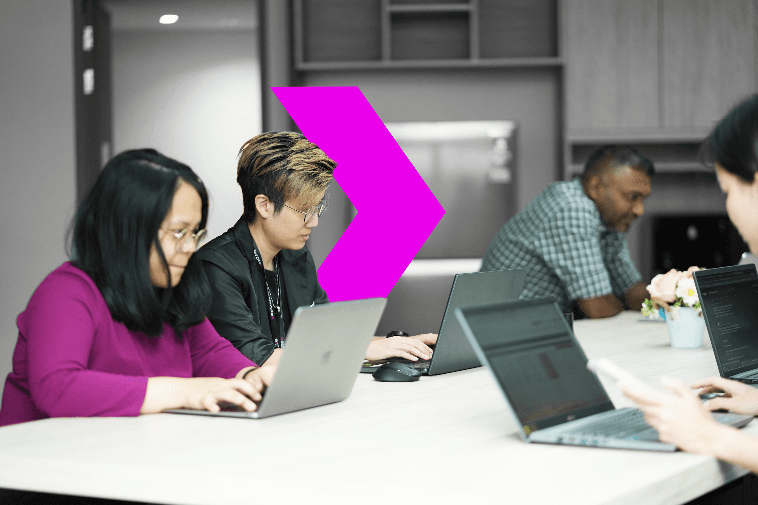 A group of individuals working on laptops at a modern conference table, with a vibrant pink arrow graphic in the background.
