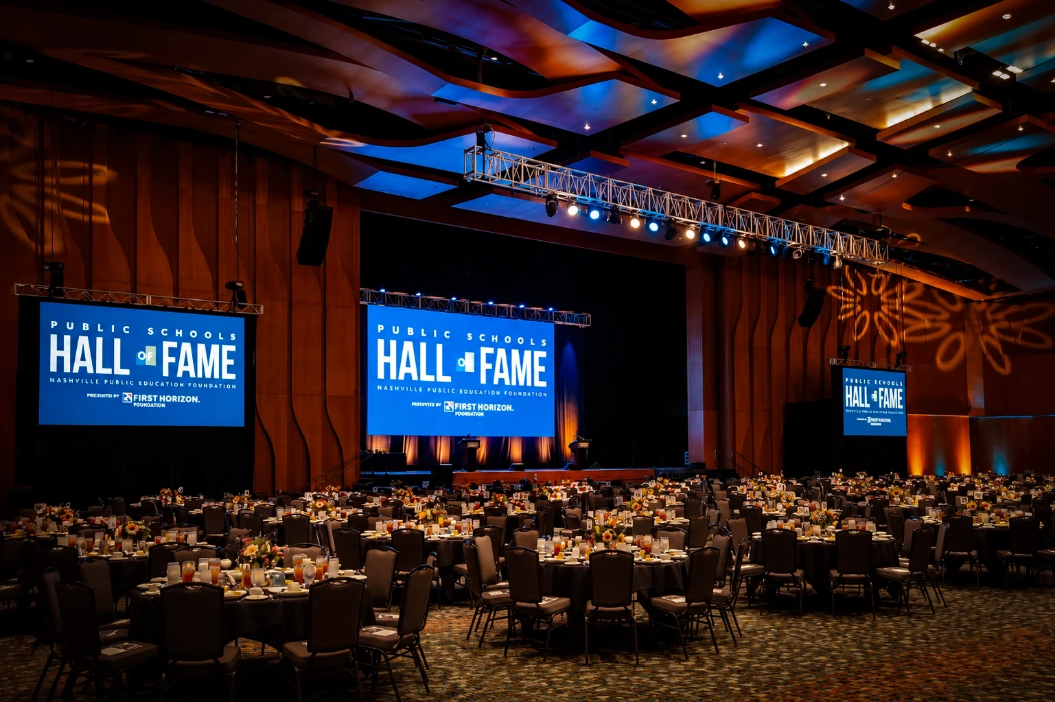 Ballroom set for dinner with 'Public Schools Hall of Fame' video walls and wood-slat ceiling at the Nashville gala — corporate event production by UpLight Technologies