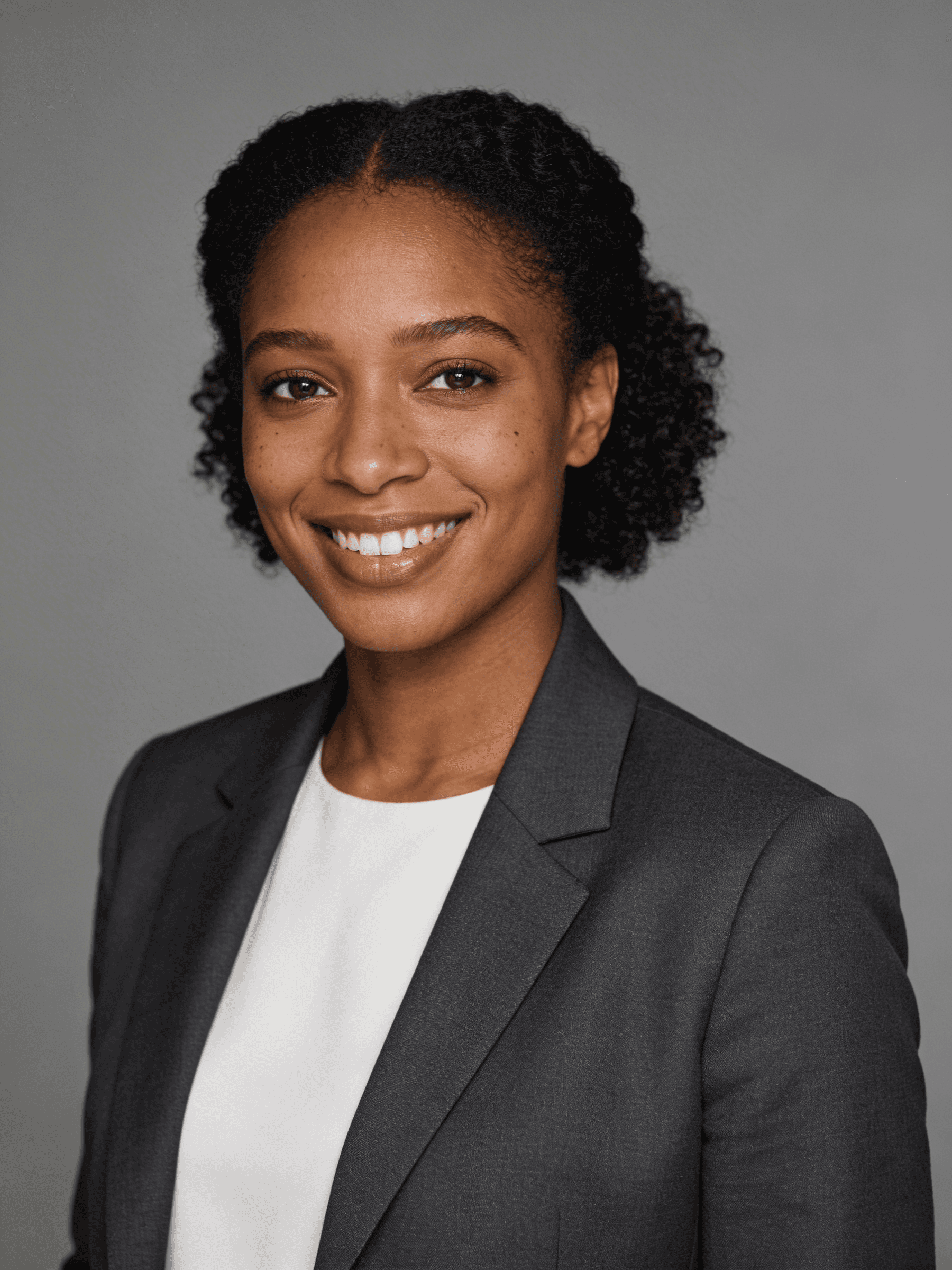 Professional portrait of a smiling individual in a gray blazer and white top, set against a neutral background.