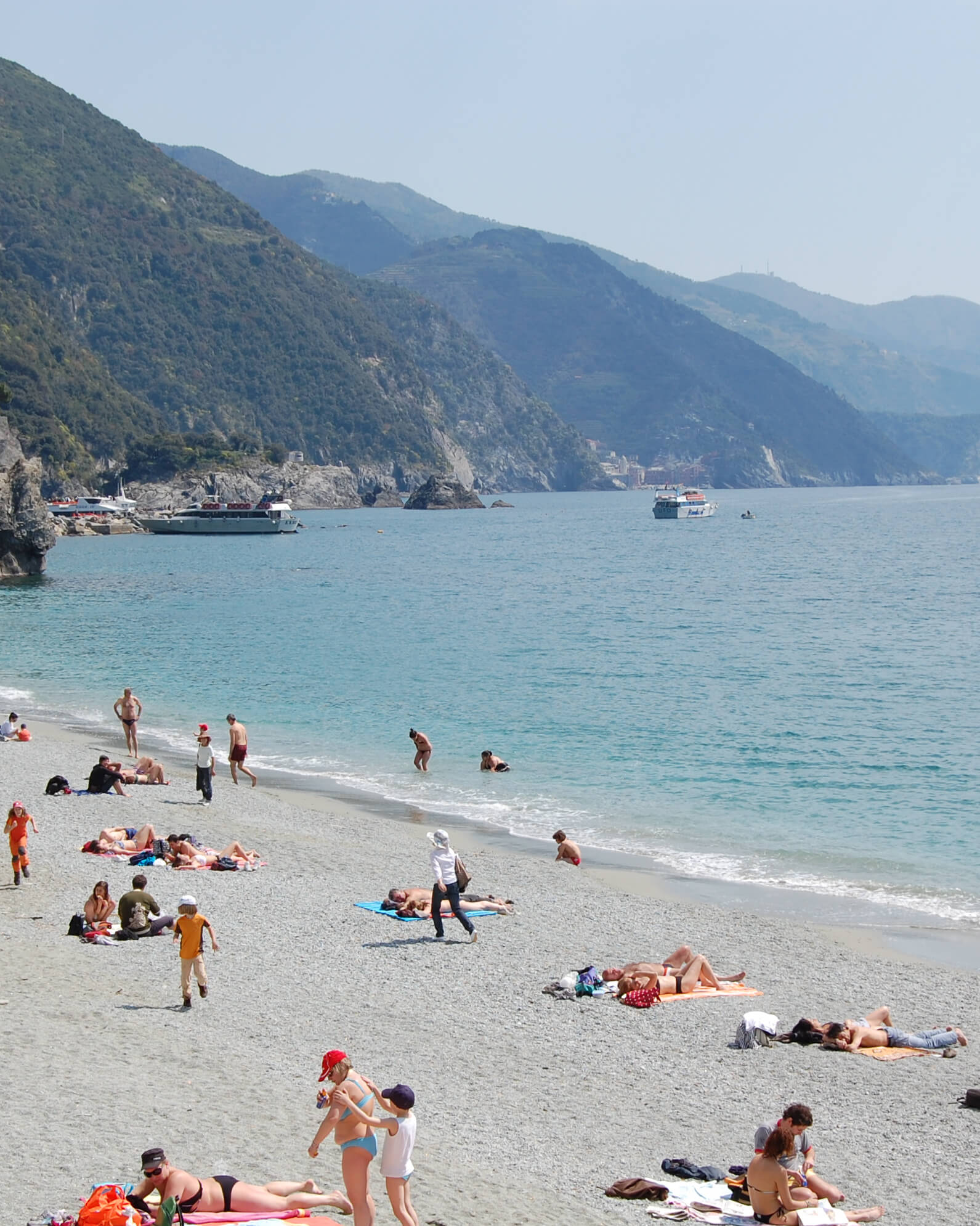 sunny beach scene with people in bright bathing suits with seaside mountains in the background