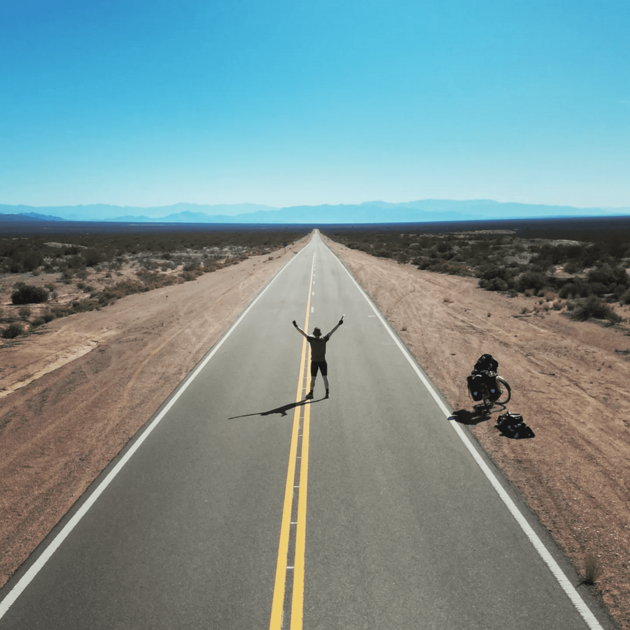 A man stands with his arms spread in triumph in the middle of an empty road in the middle of nowhere