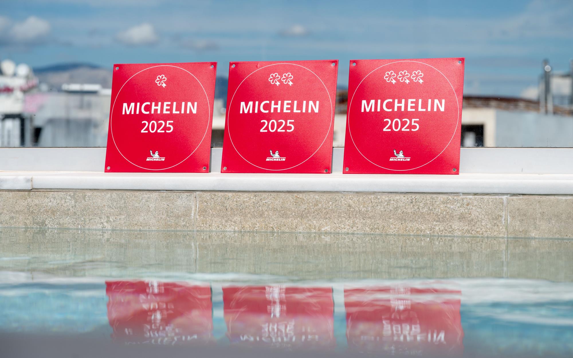 Michelin 2025 One, Two, and Three Key plaques lined up on a rooftop pool's edge.