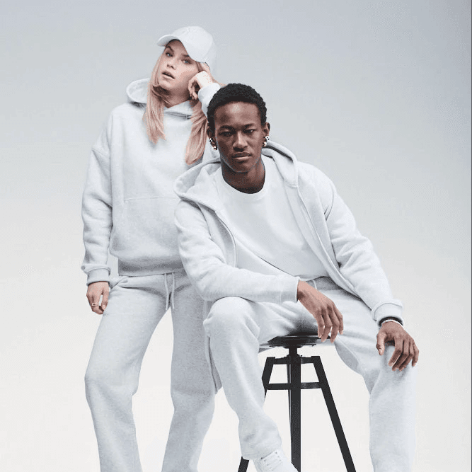 Two persons wearing matching light grey Sunday Superior sweats in a studio setting
