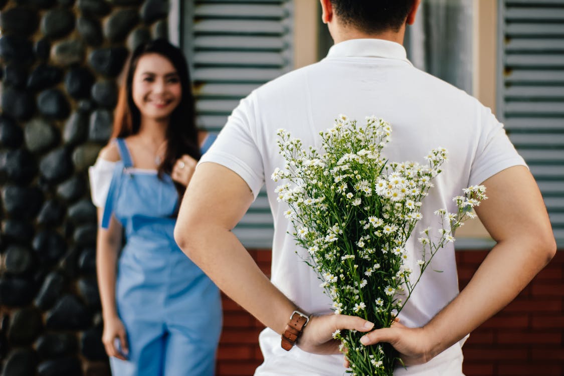 Free A man surprises his partner with flowers behind his back, symbolizing love and romance. Stock Photo