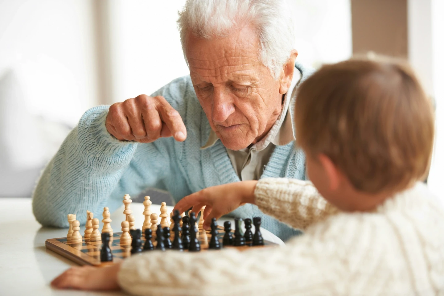 A grandfather and his grandson playing chess in a brightly lit room